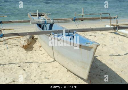 Traditionelles Auslegerkanu ruht auf einem sandigen Strand mit ruhigem blauem Ozeanwasser im Hintergrund Stockfoto