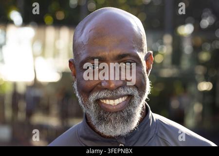 Älterer afrikanischer Mann lächelt, steht im Park, trägt eine graue Sportjacke mit Reißverschluss Stockfoto