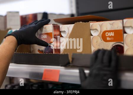 Arbeiter mit schwarzen Handschuhen, der Chai-Tee-Boxen in ein Regal im Supermarkt einräumt Stockfoto