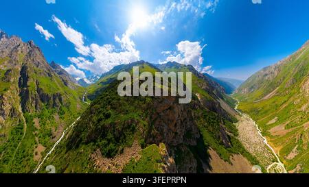 Luftperspektive zeigt majestätische Berggipfel, die von steilen Hängen und einem sich windenden Flussbett unten flankiert werden. Ein heller, sonniger Tag unterstreicht die natürliche Schönheit Stockfoto