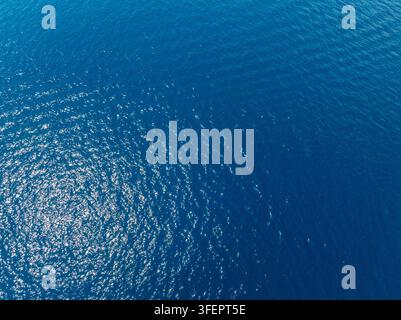 Luftbild zeigt ruhiges Meerwasser mit Sonnenlicht, das sich auf der Oberfläche spiegelt. Tiefblaues Wasser zeigt kleine Wellen, die einen abstrakten Hintergrund bilden. Stockfoto