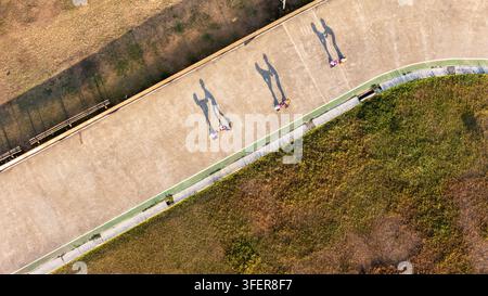 Luftaufnahme von Menschen, die einen gepflasterten Weg entlanggehen und lange Schatten auf den Boden werfen, umgeben von grasbewachsenen Flächen in Bantul, Sonderregion Yogyakarta Stockfoto
