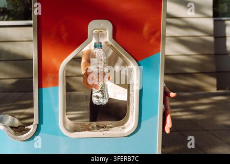 Eine Person füllt eine Plastikflasche mit Trinkwasser, während sie im Sommer in der Stadt unterwegs ist. Trinkwasser-Füllstation Stockfoto