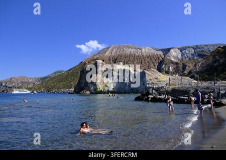 Badegäste baden im abgesperrten Schlammpool und den schwefelgasreichen Gewässern vor der Insel Vulcano, Äolische Inseln, Sizilien, Italien. Der Zugang zum Thermal-Schlammbereich wurde eingeengt, nachdem Überwachungen Temperaturen der Fumarolen gezeigt hatten, die höher waren als in früheren Jahren, was die Behörden veranlasste, die nutzbare Oberfläche aus Sicherheitsgründen zu begrenzen. Trotz des engeren Umkreises nutzen Besucher den Ort weiterhin wegen seiner angeblichen therapeutischen Eigenschaften und waten in flachen, warmen Gewässern, in denen vulkanische Gase an die Oberfläche sprudeln. Stockfoto