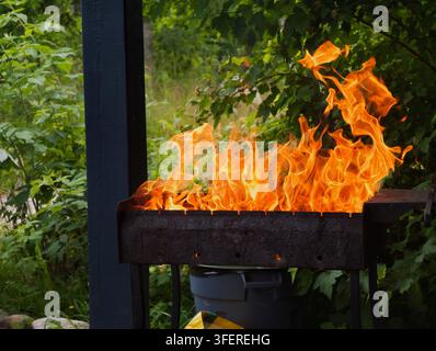 Brennendes Holz und Holzkohle mit einer hellen orangefarbenen Flamme in einem Metallgrill. Die Holzscheite und Kohlen brennen im Grill und erzeugen Hitze. Flammen umgeben Stockfoto