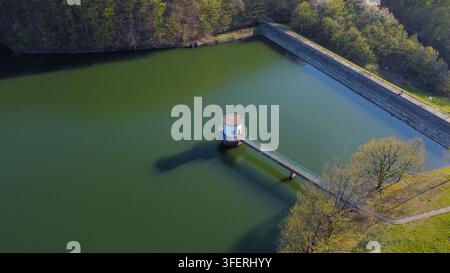 Luftbild des Bovan-Sees mit seinem markanten Wasserentnahmeturm, der durch einen schmalen Steg verbunden ist, umgeben von üppigen grünen Bäumen und ruhigem Wasser in Stockfoto
