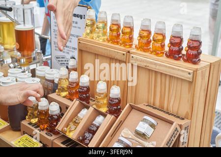Eine Nahaufnahme verschiedener roher Honigvariationen in niedlichen, bärenförmigen Flaschen, die auf Holzkisten auf einem Markt ausgestellt sind Stockfoto
