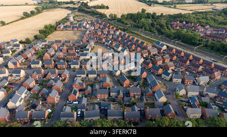 Drohnen-Luftaufnahme einer modernen Wohnsiedlung, umgeben von landwirtschaftlichen Feldern und Landschaft in England während Stockfoto