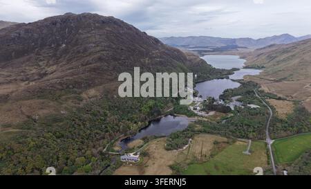 Luftaufnahme von Kylemore Abbey, eingebettet in die raue Landschaft, umgeben von üppigen grünen Hügeln, dunklen Seen und gewundenen Straßen in Connemara, County Galway Stockfoto