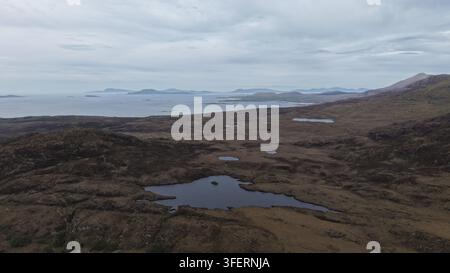 Luftbild der rauen Moorschlandschaft mit kleinen Seen und entfernter Küstenlinie unter einem bewölkten Himmel in Woodlawn, County Galway, Irland. Stockfoto