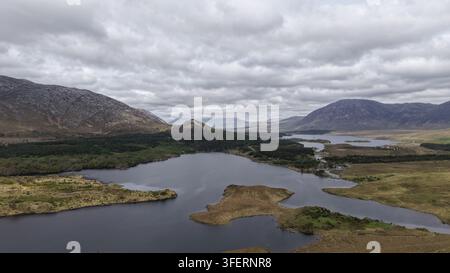 Luftbild der rauen Connemara-Landschaft mit dunklen Seen, sanften Hügeln und weitläufigen Mooren unter einem bewölkten Himmel in Woodlawn, County Galway, Irland Stockfoto