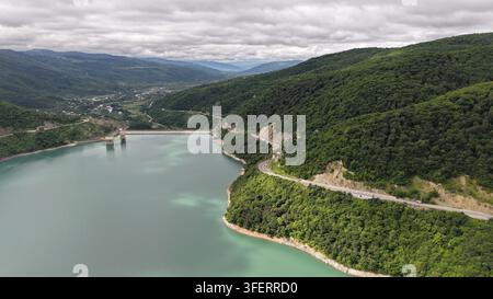 Luftaufnahme des Zhinvali-Stausees und der sich schlängelnden georgischen Militärstraße, umgeben von üppigen grünen Bergen unter einem bewölkten Himmel in Ganisi, Mtskheta Stockfoto