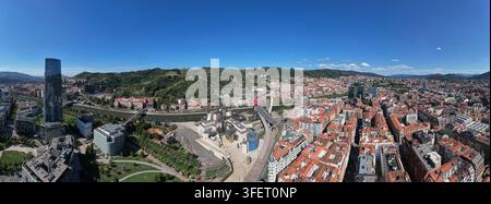 Luftaufnahme des Guggenheim Museums Bilbao, das entlang des Nervión-Flusses mit der umgebenden urbanen Architektur und grünen Hügeln in Bilbao, Baskenland, liegt Stockfoto