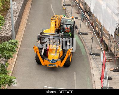 Teleskopbagger bewegt Materialien neben Gerüsten während Renovierungsarbeiten sicher. Stockfoto