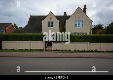 Ein cremefarbenes zweistöckiges Vorstadthaus in Northampton mit gestutzten Hecken, einem beigen Zaun und Vorgartenblumen, gesehen von der Straße aus unter einer bewölkten Stockfoto
