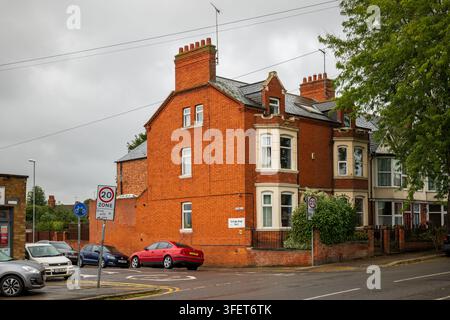 Eckreihenhaus aus rotem Backstein in Northampton mit geparkten Autos, 20-Mph-Verkehrsschild und bewölktem Himmel, das typische britische Wohnarchitektur zeigt Stockfoto