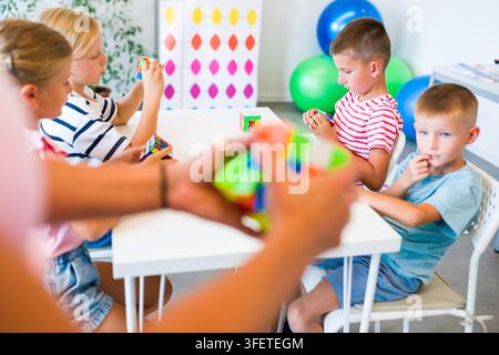 Kinder in einer mentalen Arithmetikstunde üben mit ihrem Lehrer das Lösen von Würfelpuzzles, um Konzentration, Gedächtnis, räumliches Denken und Problemlösungsfähigkeiten zu entwickeln Stockfoto