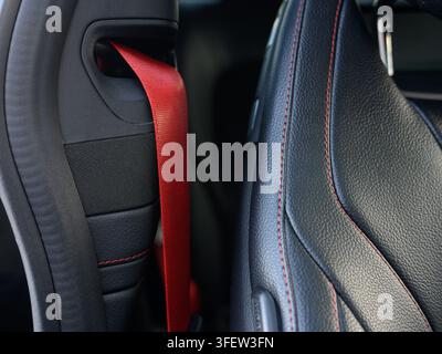 Roter Sicherheitsgurt schlingt sich durch die Autositztasche. Schwarze Ledersitze zeigen rote Nähtdetails. Nahaufnahme des Sicherheitsmerkmals im Fahrzeuginnenraum. Perfekt Stockfoto