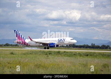 SKY express Airbus A320neo-Passagierflugzeug landet auf der Landebahn mit Reifenrauch unter bewölktem Himmel, Berge im Hintergrund. Stockfoto