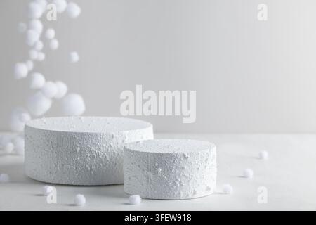 Zwei weiße, strukturierte Podeste mit verstreutem Schnee auf minimalem Winterhintergrund für Weihnachtsprodukt-Mockup oder Kosmetikpräsentation Stockfoto