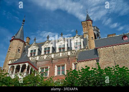 Verschnörkelte mittelalterliche gotische Fassade des Gruuthuse Museums in Brügge Belgien mit Ziegeltürmen roten Fensterrahmen und grünem Laub unter blauem Himmel. Stockfoto