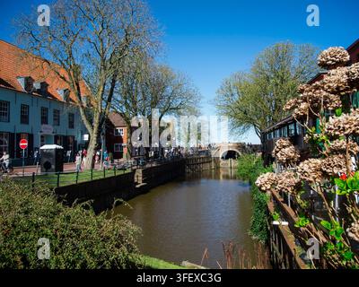 Lebhaft und doch entspannter Fußgängerverkehr in der Fußgängerzone neben dem alten Schleusenbecken in Greetsiel, Ostfriesland, mit dem Tor geschlossen unter einem Clou Stockfoto