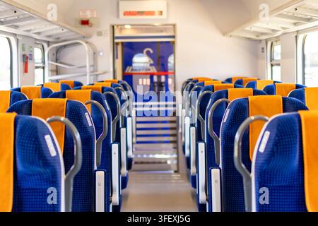 Leerer Zugwaginnenraum zeigt Reihen von blauen und orangefarbenen Sitzen, die sich nach vorne erstrecken. Konzept von modernem öffentlichen Nahverkehr und sauberem Zug Stockfoto