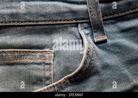 Nahaufnahme der vorderen Tasche einer blauen Jeans mit Nähten. Detaillierte Textur des klassischen blauen Denimstoffs, der die vordere Tasche, die Münztasche und die Gürtelschlaufe zeigt, und orange Stockfoto