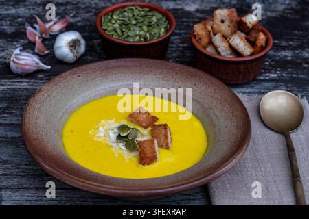 Kürbiskremesuppe mit Croutons und Samen in einer Keramikschüssel. Köstliche gelbe Kürbispüreesuppe serviert mit knusprigen Croutons, Kürbiskernen und Knoblauch Stockfoto