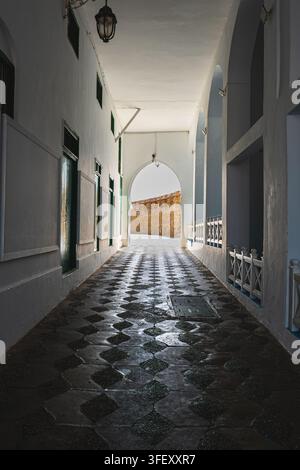 Perspektivische Ansicht einer sauberen historischen Gasse, die zu einem eleganten gewölbten Eingang in der alten Medina von Asilah, Marokko, führt Stockfoto