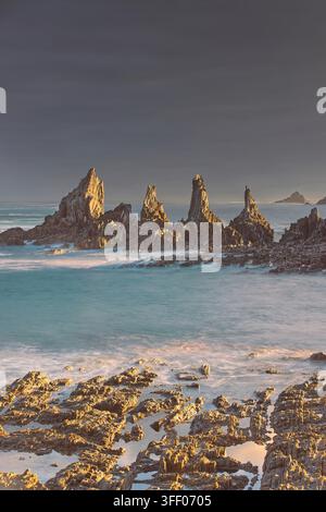 060 Das warme Licht der Morgendämmerung erhellt die Kliffspitzen von La Forcana am Strand von Playa Gueirúa, der Himmel ist von einer dicken dunklen Wolke bedeckt. Cudillero-Asturien-Spanien. Stockfoto