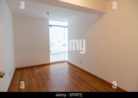 Leere moderne Raum: Ein leerer Raum mit polierten Holzböden und weißen Wänden, mit einer Glastür, die zu einem hellen, offenen Raum führt. Stockfoto