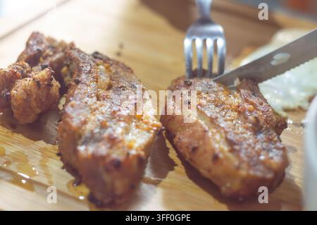 Knusprige Schweinebauch-Häppchen: Nahaufnahme von herzhaften, knusprigen Schweinebauchstücken, die vor Saft glänzen und bereit sind, genossen zu werden, mit einer Gabel und einem Messer bereitgehalten Stockfoto