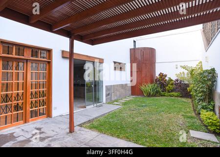 Moderne Innenhof-Oase: Ein heller und luftiger Innenhof zeigt einen üppigen grünen Rasen, eine hölzerne Pergola und moderne architektonische Elemente Stockfoto