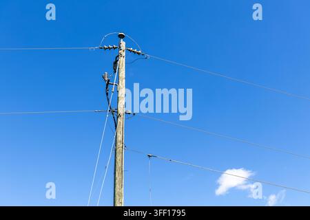 Hölzerner Strommast und Freileitungen stehen vor einem lebhaften blauen Himmel mit einer kleinen weißen Wolke im ländlichen Virginia, USA. Stockfoto