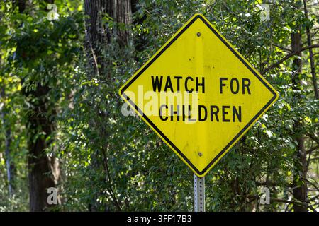 Abgenutztes gelbes „VORSICHT VOR KINDERN“-Warnschild steht neben einer bewaldeten Landstraße in Virginia, USA. Stockfoto