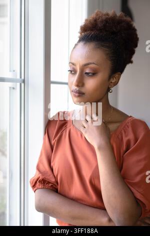 Nachdenkliche junge Afrikanerin am Fenster stehend Stockfoto