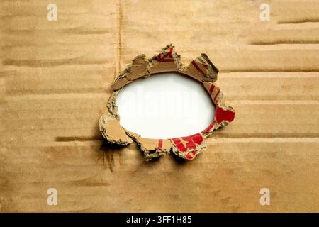 Ein zerfetztes, kreisförmiges Loch, das durch eine braune Wellplattenplatte gerissen wurde, zeigt einen leeren weißen Hintergrund. Perfekt zum Einrahmen von Nachrichten, Kopierraum Stockfoto