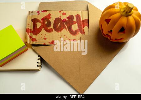 Eine Ansicht von oben auf ein Stück Pappe mit dem Wort Tod, das in rotem Blut geschrieben ist, in einem braunen Umschlag, neben einem kleinen Jack-o'-Lantern und einem Notizblock Stockfoto