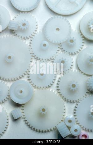 Hochwinkelansicht verschiedener kleiner weißer Plastikzahnräder und Zahnräder, die auf einer hellen Oberfläche verstreut sind, ideal für Ingenieur- und Hobbykonzepte Stockfoto