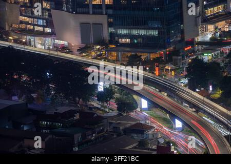 Hochwinkel-Nachtansicht einer erhöhten Autobahn mit Lichtspuren von Ampeln, die sich durch eine modern beleuchtete Stadt Jakarta schlängeln. Stadtkulissen-Hintergrund Stockfoto