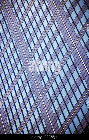 Moderne Hochhausfassade schräg aufgenommen, betont wiederholte rechteckige Fenster, starke Linien und urbanes Architekturmuster. Stockfoto