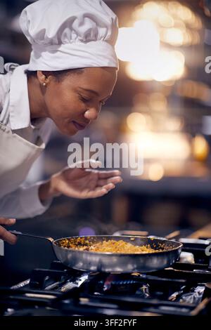 Frau genießt das Kochen der Mahlzeit. Kochen in professioneller moderner Küche, Restaurantkonzept Stockfoto