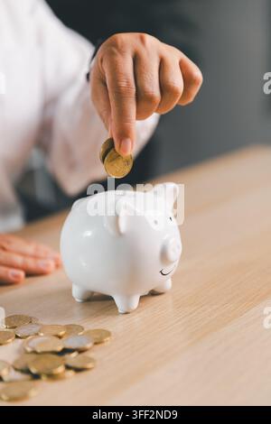 Nahaufnahme eines Gesundheitsfachpersonals, das eine Münze in ein Sparschwein neben Ersparnissen einwirft, was medizinische Budgetierung, Krankenversicherung und Notfälle darstellt Stockfoto