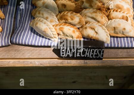 Frisch gebackene Schinken-Käse-Empanadas, die zum Verkauf auf einem Holzstand auf einem lokalen Straßenfest ausgestellt sind und Besucher mit einem herzhaften Snack locken. Stockfoto