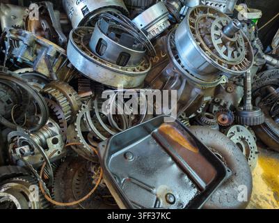 Nahaufnahme eines großen Haufens zerlegter Automobilgetriebekomponenten. Verschiedene Gänge, Kupplungen und Drehmomentwandler sind sichtbar und zeigen ihre abgenutzten und schmierigen Texturen. Stockfoto