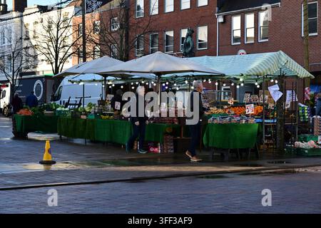 Lichfield, UK - 10. Dezember 2025: Händler verkaufen Obst und Gemüse unter Baldachinen auf einer belebten Kopfsteinpflasterstraße Stockfoto