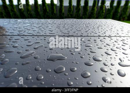 Wassertropfen auf einem wetterfesten Komposit-Gartentisch mit grünem Zaun im Hintergrund Stockfoto