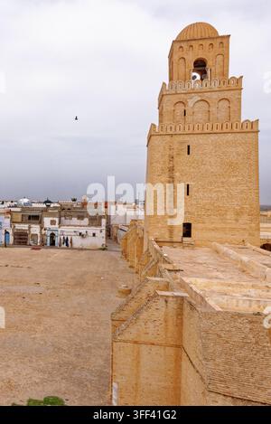 Hohe Blickwinkelansicht des massiven steinernen Innenhofs, des quadratischen Minaretts und der dekorativen Kuppeln der historischen Großen Moschee von Kairouan unter einem bewölkten Himmel Stockfoto