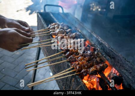 Koch grillt indonesisches Sate Klatak-Ziegenfleisch auf Metallspießen über flammendem Holzkohle, authentisches Straßenfood aus Yogyakarta. Stockfoto